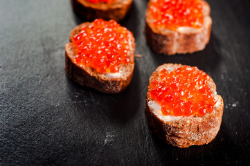 Red caviar on bread on slate background.