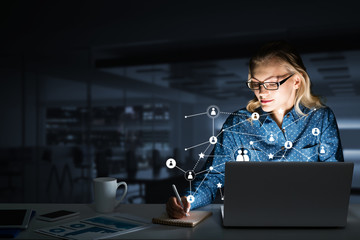 Attractive blonde wearing glasses in dark office using laptop. Mixed media