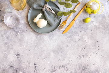 Beautiful Easter table setting in Scandinavian style. Green mint plate with bunny, painted  egg and  cold cutlery on modern concrete background decorated with plant. Copy space.Top view