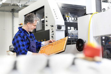 Introligatornia, mężczyzna drukarz przy maszynie  montuje wykrojniki 
