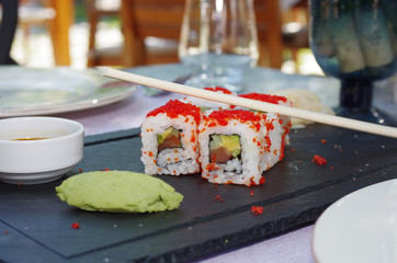 Close up view of a sushi served on a black plate with sauce and sticks