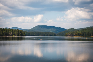 Beautiful summer landscape - calm waters of a lake and a boat. Green forest and mountain in the background. Bulgaria.