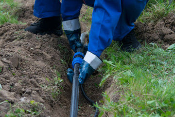 hands of the worker, in blue gloves, laid a plastic pipeline in an open trench in the ground