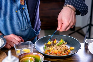 Chef decorates the buckwheat noodles on wok and baked carp. Master class in the kitchen. The process of cooking. Step by step. Tutorial. Close-up