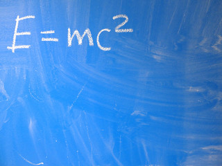 Mathematical formula e=mc2 squared written on a blue, relatively dirty chalkboard by chalk. Located in the upper left corner of the image making space for some message or note on the board.