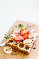 Belgian waffle with fruit and chocolate sauce is beautifully served on a wooden board. Top view, flat lay