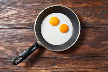 Fried eggs in a frying pan on a wooden background with copy space. Breakfast from natural fresh products. Top view.