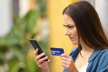 Fototapeta premium Angry woman paying with credit card and smart phone outdoors