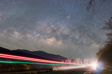 Night shot of Milky way in the great Universe over the road.Light from the cars that runs through the bridge on the road at night among the stars and Milky Way in dark sky. © Tanongsak