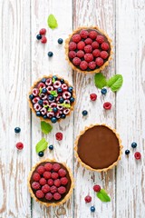Raspberry and blueberry tartlets with chocolate ganache, fresh berries and mint leaves, selective focus. Fresh fruit tart on white background, freshly homemade fruit cake on a table