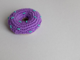 Knitted purple donut on the gray background is sewed from fabric for a children's game in a shop or cafe.