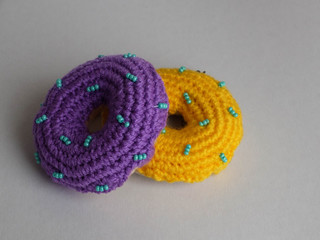Obraz premium Knitted purple and yellow donuts on the gray background is sewed from fabric for a children's game in a shop or cafe.