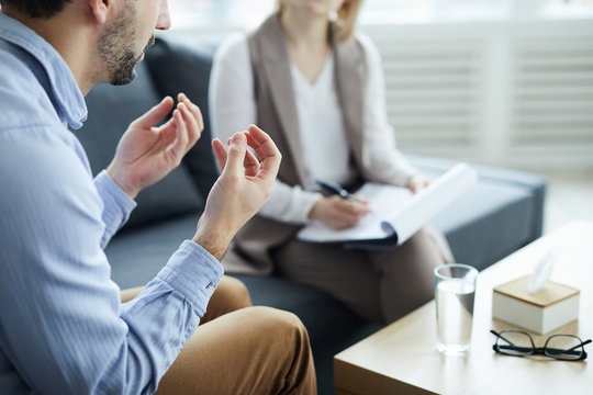Young man explaining his problems to counselor while sitting in front of her by table with glass of water on edge