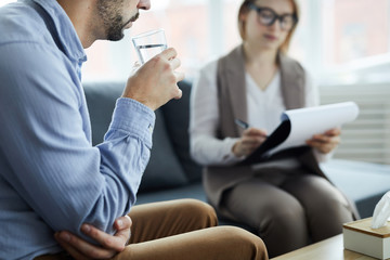 Troubled patient of counselor having glass of water while discussing his problems during...
