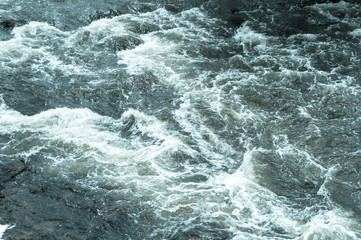 Fototapeta na wymiar Turbulent stream, fast flowing river with blue water and white foam waves, background, top view