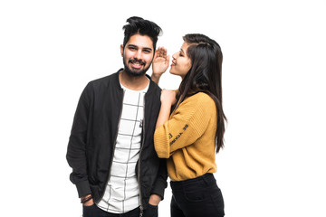 Beautiful indian couple, woman whispering to boyfriends ear isolated on gray background