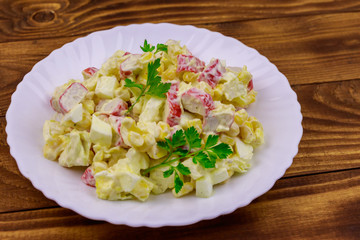 Salad with crab sticks, sweet corn, chinese cabbage, eggs and mayonnaise on wooden table