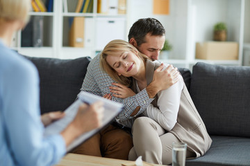 Young couple sitting on couch in embrace after consulting with counselor and solving their problem