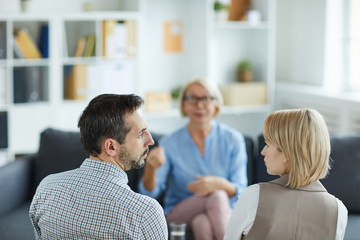 Rear view of young displeased husband and wife looking at one another while visiting counselor