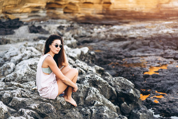 Pretty long hair brunette tourist girl relaxing on the stones near sea.