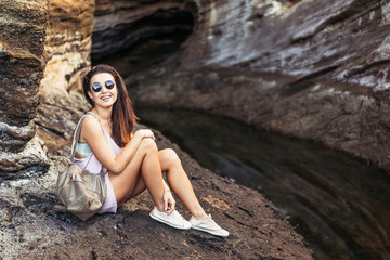 Obraz premium Pretty long hair brunette tourist girl relaxing on the stones near sea.