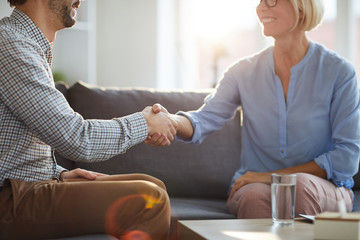 Obraz premium Successful counselor shaking hand of mature female patient while both sitting on couch after consultation