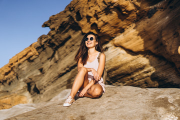 Pretty long hair brunette tourist girl relaxing on the stones near sea.