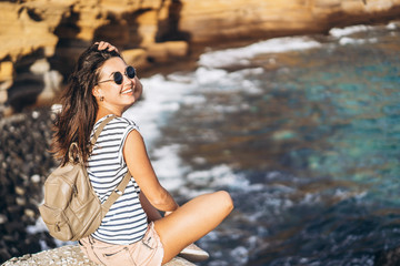 Pretty long hair tourist girl relaxing on the stones near sea.