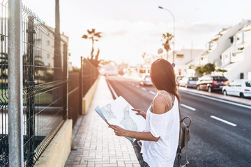 Pretty brunette tourist girl with map in hands on the street searching way.