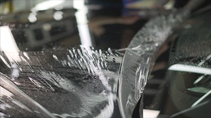 professional applying protective film to the red car. Master glues a protective film on the hood of...