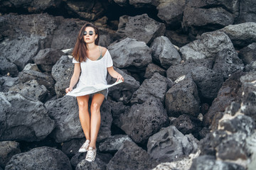 Pretty long hair tourist girl relaxing on the stones near sea.