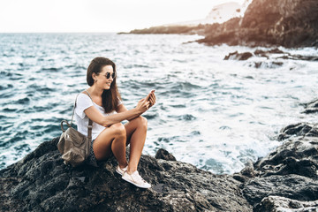 Pretty long hair tourist girl relaxing on the stones near sea.
