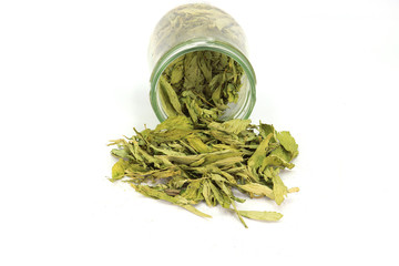Dried Stevia ( Stevia rebaudiana Bertoni) leaves poured out of a glass jar isolated on white background.