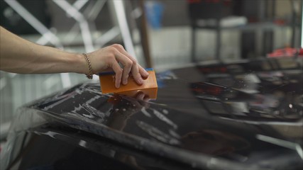 professional applying protective film to the red car. Master glues a protective film on the hood of the car