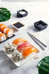 Various sushi on ceramic plate with metal Korean sticks on light stone background with green leaves, flat lay copy space