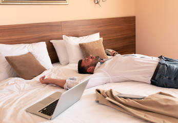 Young businessman lying on hotel bed exhausted from the business trip.