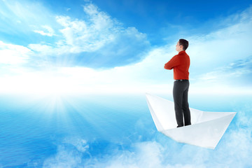 Obraz premium Handsome asian businessman standing on paper boat sailing on blue ocean