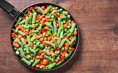 Mixed vegetables. green beans, peas and carrots in an iron pan on a wooden background