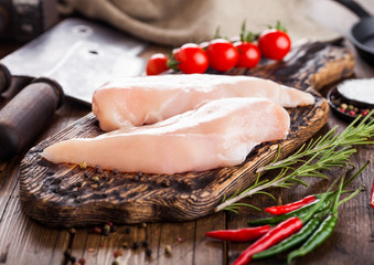 Fresh Raw Organic Chicken Fillet Breast on vintage board with meat hatchets and spices with herbs on wooden background. Tomatoes and pepper.
