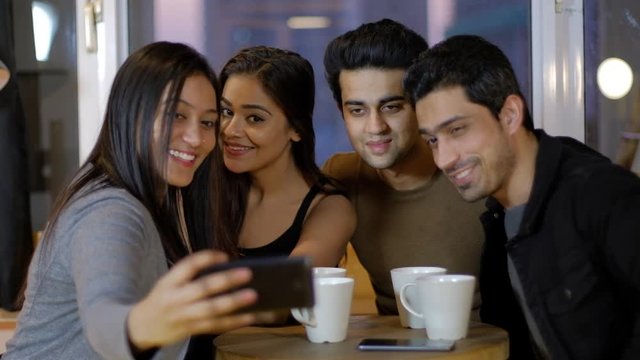 Young friends smile and pout for selfie photos from a mobile phone as they huddle together and then review and discuss about the photo taken and smile