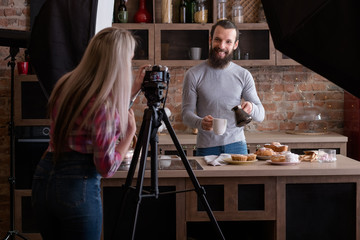 Lifestyle photographer at work. Woman shooting young man at loft kitchen. Coffee and pastries. Backstage photography.