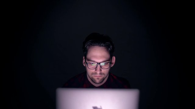 Hacker focused to work on computers at night in a dark room. Portrait of a man behind the monitor in the dark. 