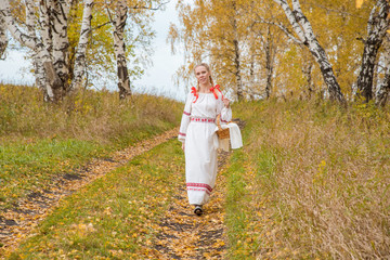 Beautiful girl in a traditional Slavic dress with a straw basket in her hands walks in the autumn forest
