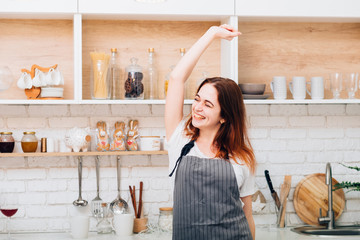 Happy housewife. Cooking fun and pleasure. Young female wearing apron dancing in kitchen.