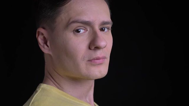 Close-up portrait in profile of middle-aged concentrated caucasian man in yellow sweater watching seriously into camera on black background.