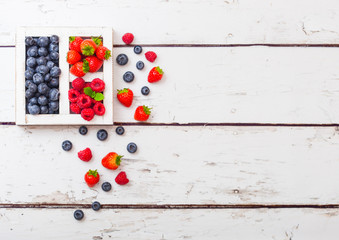 Fresh raw organic berries  in white vintage wooden box on wooden background. Space for text. Top view. Strawberry, Raspberry, Blueberry and Mint leaf
