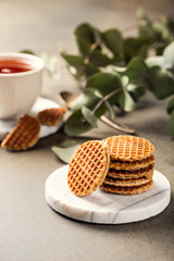 Mini stroopwafel, syrupwaffles cookies with cup of tea and eucalyptus twigs on light background with copy space.