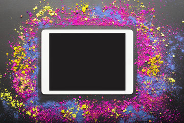 Touchpad on colorful holi powder background. Touchscreen computer on festive holi colors...