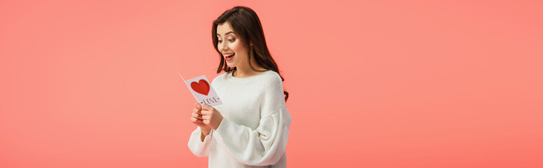 panoramic shot of surprised young woman holding card with love lettering isolated on pink