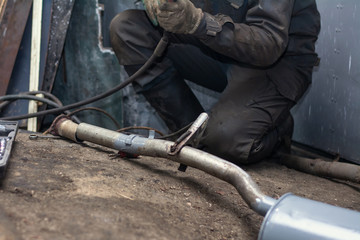 repairing of corrugation muffler of exhaust system in car workshop - serviceman welds the old...
